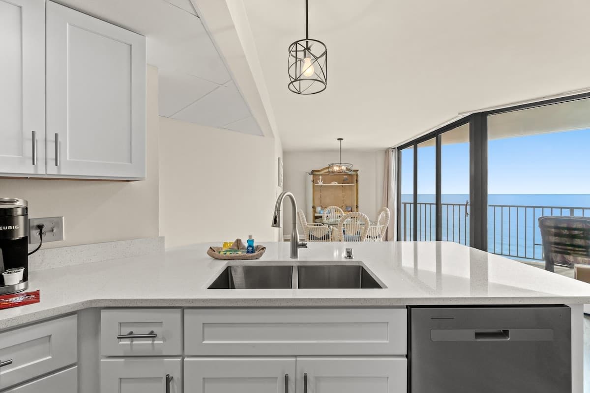 Aquavista 804E – Modern kitchen with a large island, water view, and dining area featuring wicker chairs.