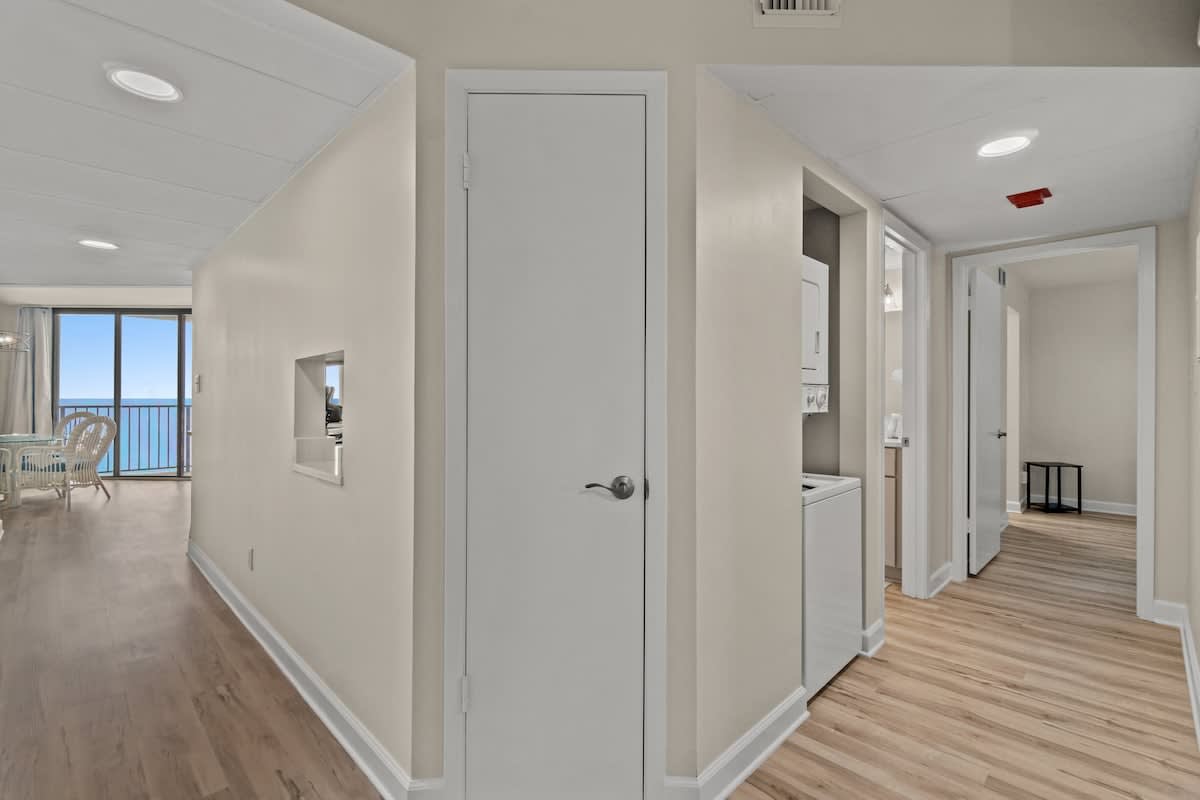 Aquavista 804E – Hallway view with laundry closet, leading to a dining area and ocean view through glass doors.