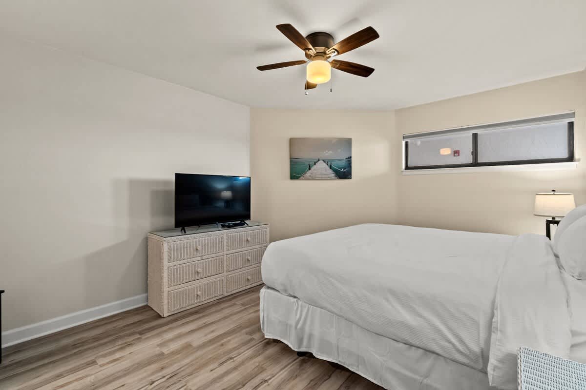 Aquavista 804E – Bedroom with a bed, television, dresser, and window featuring coastal artwork.