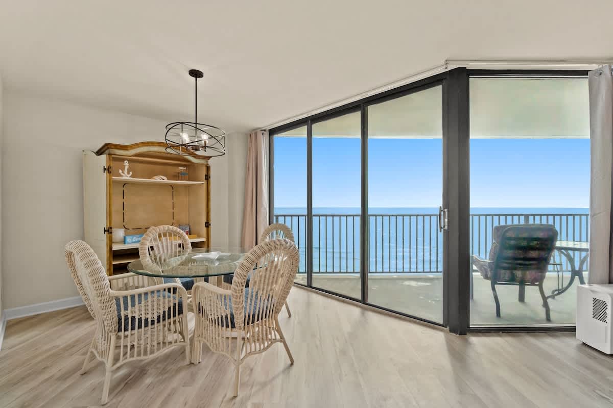 Aquavista 804E – Dining area with wicker chairs, glass table, and ocean view through large sliding glass doors.