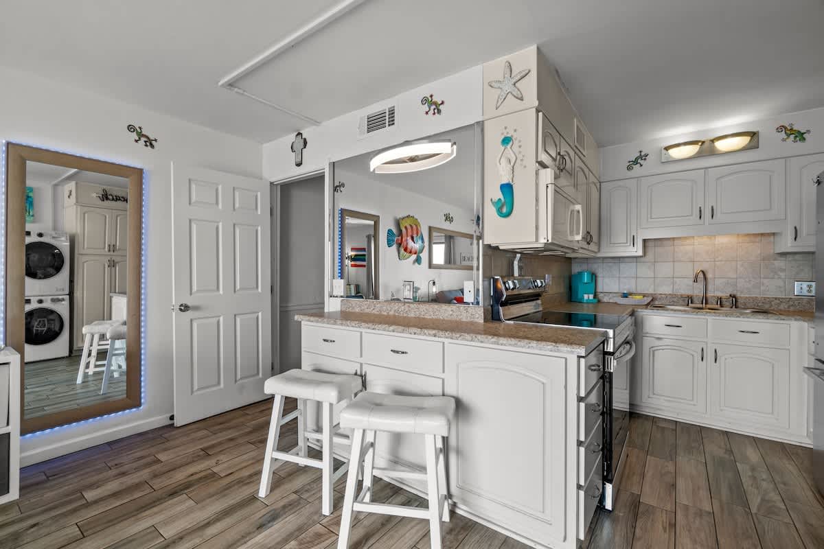 The Summit 1213 – Bright kitchen with white cabinetry, granite countertops, two bar stools, and laundry area visible through a doorway.