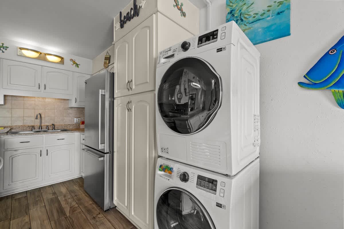 The Summit 1213 – Compact kitchen area featuring white cabinets, stainless steel fridge, and stacked washer/dryer with decorative wall art.