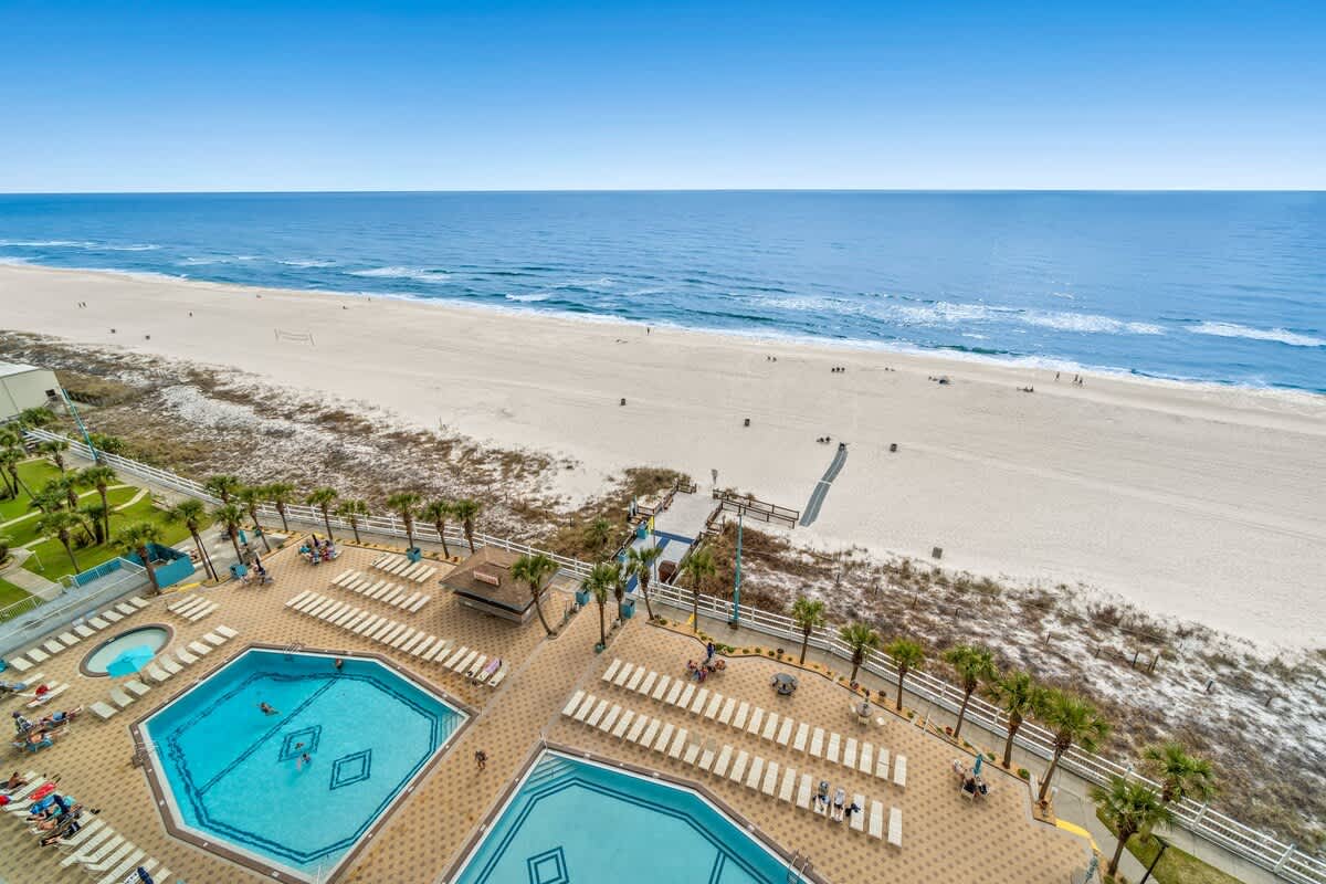 The Summit 1213 – View of pools, sun loungers, and beach with ocean in the background from a high vantage point.