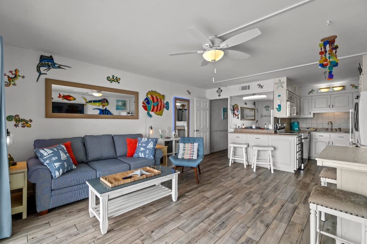 The Summit 1213 – Living room with blue sofa, white kitchen island, colorful fish decor, and wood flooring.