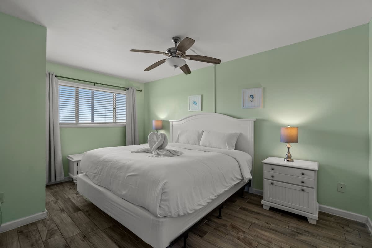 The Summit 1213 – Bright green bedroom with a king bed, ceiling fan, and window with blinds.
