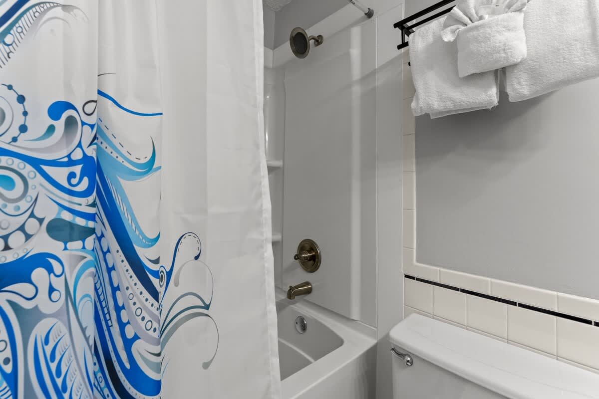 Top Of The Gulf 306 – Bathroom with shower/tub combo, decorative blue shower curtain, and stacked towels on a rack.