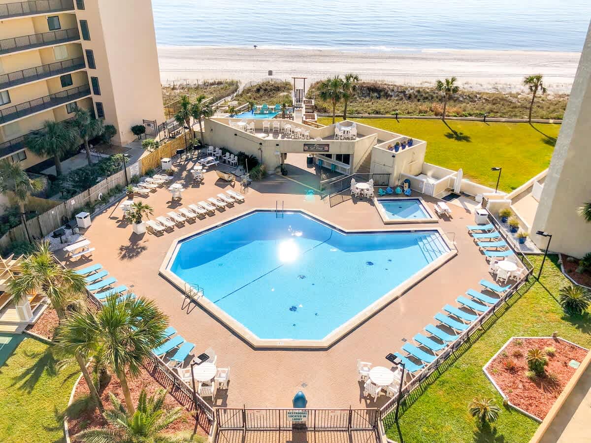 Top Of The Gulf 306 – Aerial view of an octagonal pool surrounded by loungers and a grassy area near the beach.