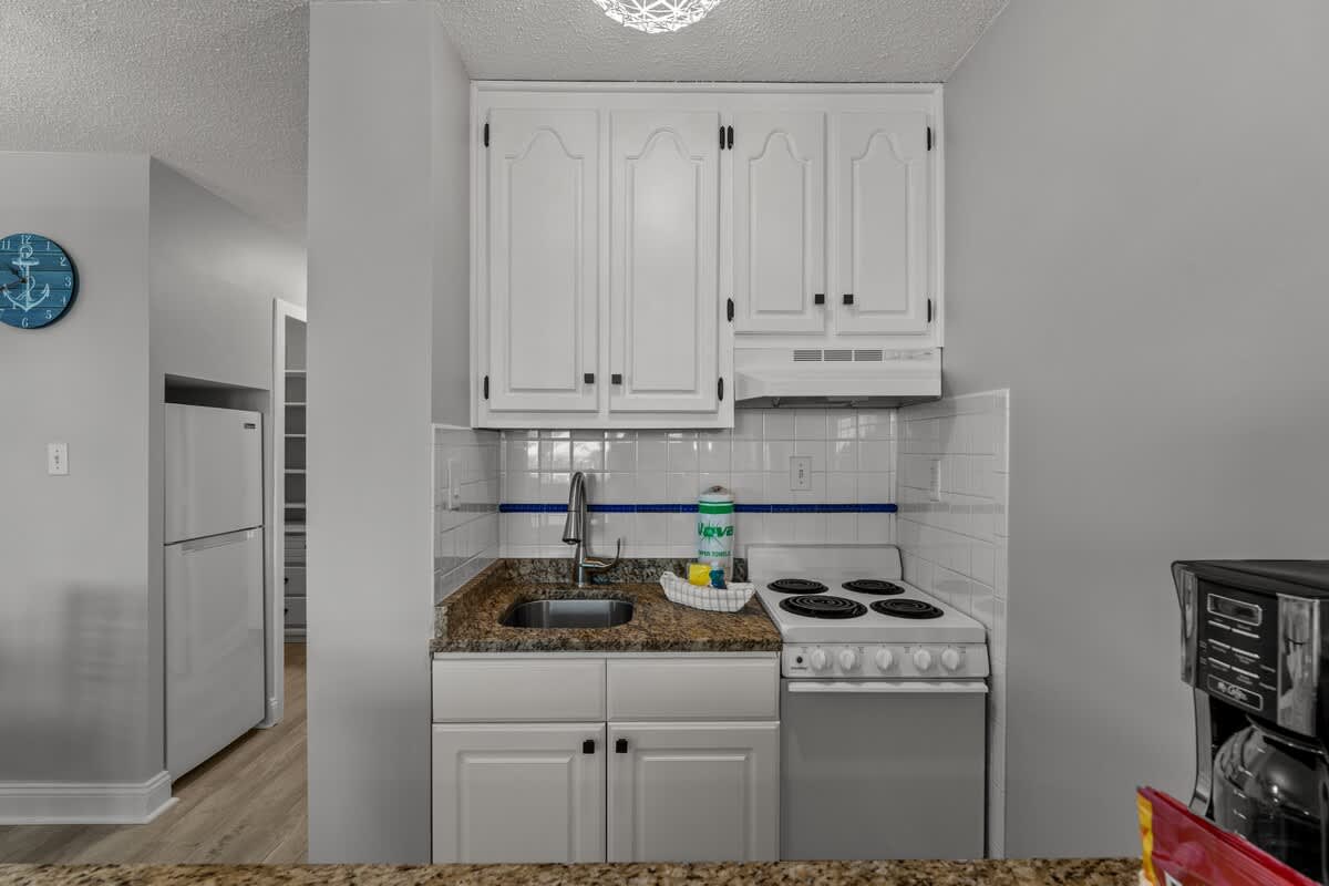 Top Of The Gulf 306 – Compact kitchen with white cabinets, granite counter, stove, sink, and coffee maker.