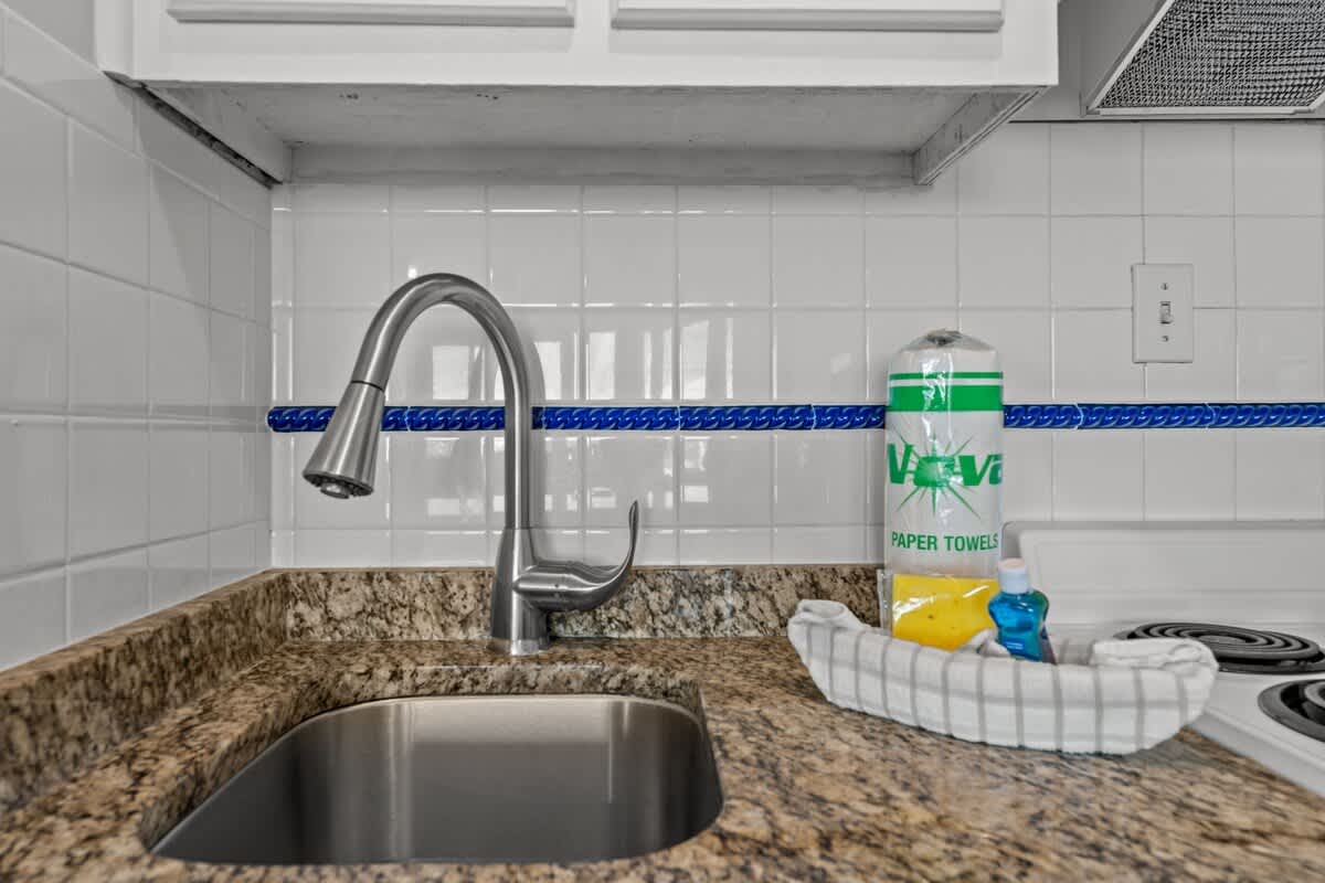 Top Of The Gulf 306 – Kitchen sink with stainless steel faucet, granite counters, paper towels, and cleaning supplies on the countertop.