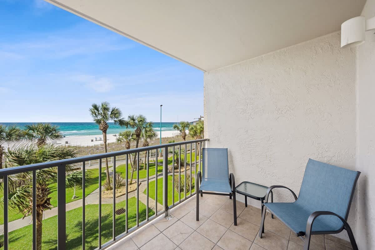 The Summit 307 – Balcony with two blue chairs and a table, overlooking the beach and ocean with palm trees.