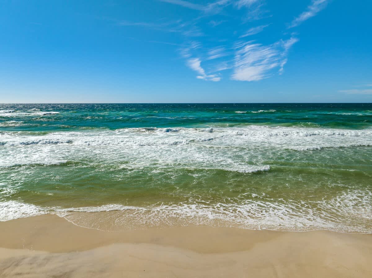 The Summit 307 – Ocean view from a beachfront location with waves crashing on sandy shore under a clear blue sky.