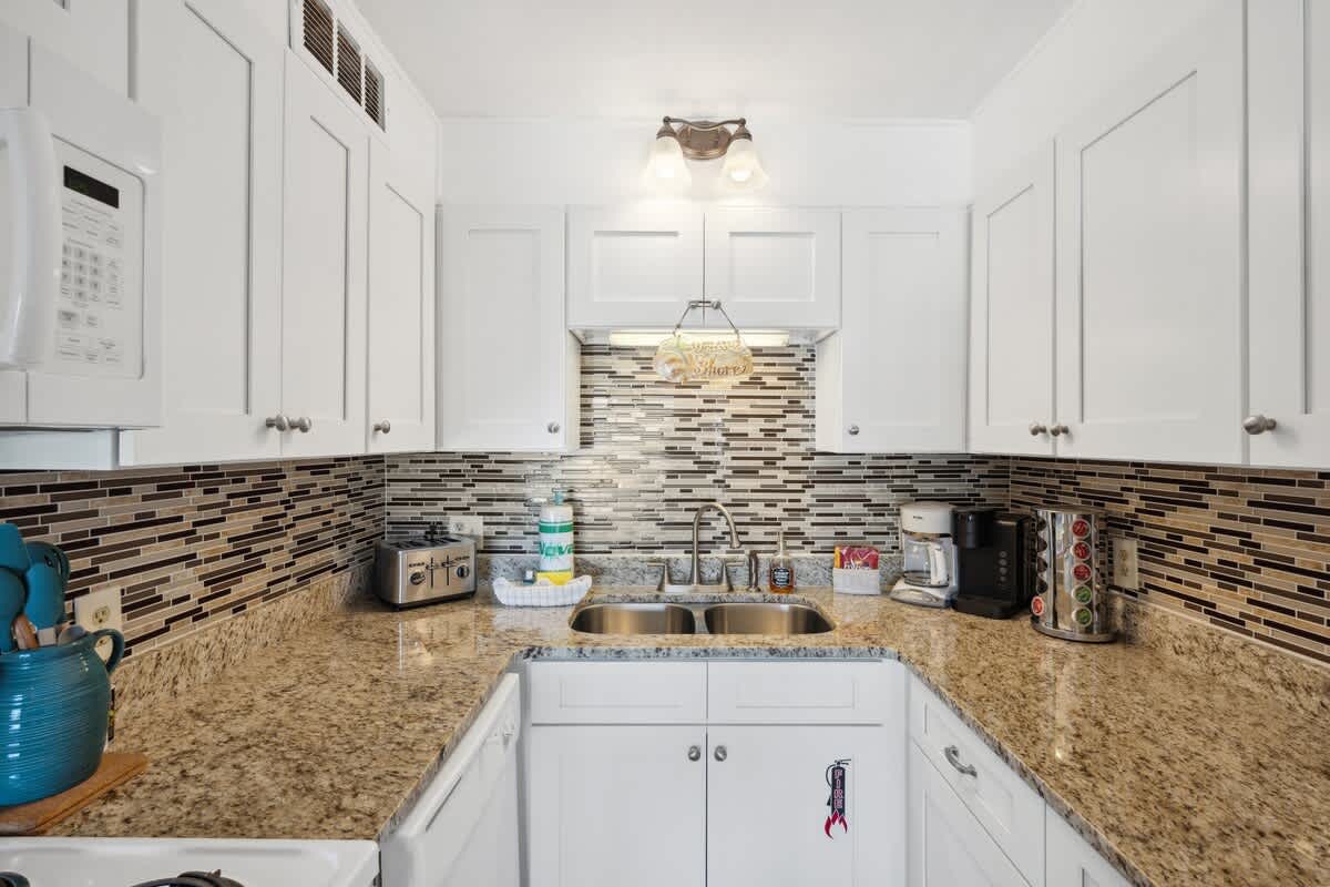 The Summit 307 – Modern kitchen with white cabinets, granite countertops, stainless steel appliances, and mosaic tile backsplash.