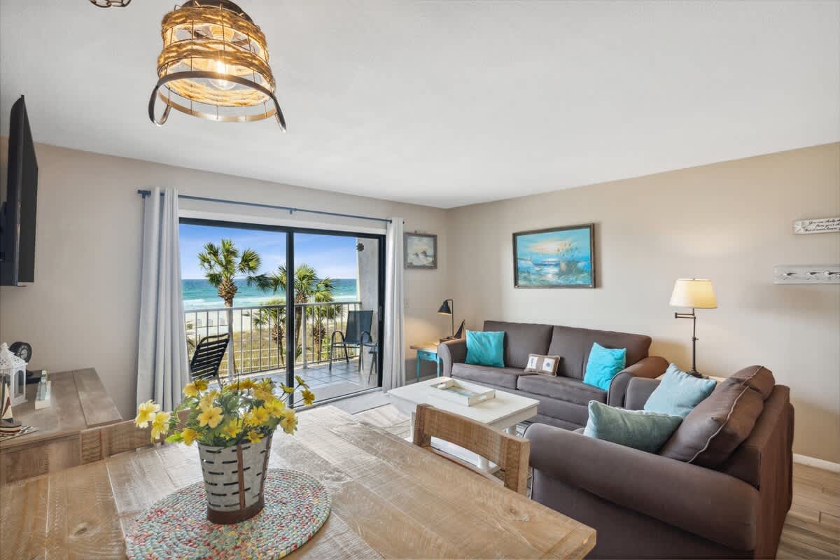 The Summit 307 – Living room with two sofas, dining table, and balcony view of palm trees and ocean.