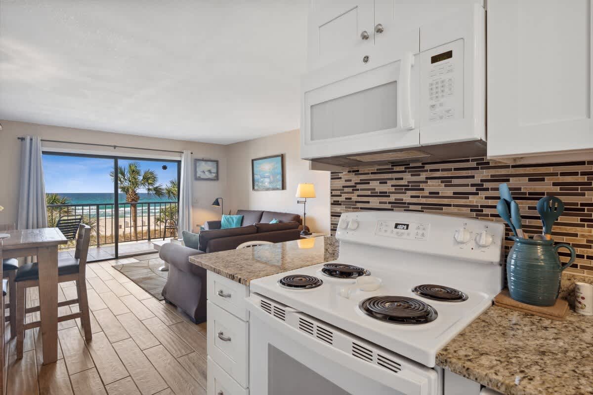 The Summit 307 – Cozy kitchen area with stove, granite countertops, and open view of palm trees and ocean through sliding glass doors.