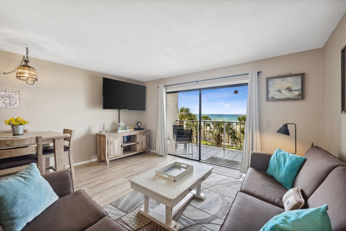 The Summit 307 – Living room with balcony view of the beach, sofa, dining table, and a TV mounted on the wall.