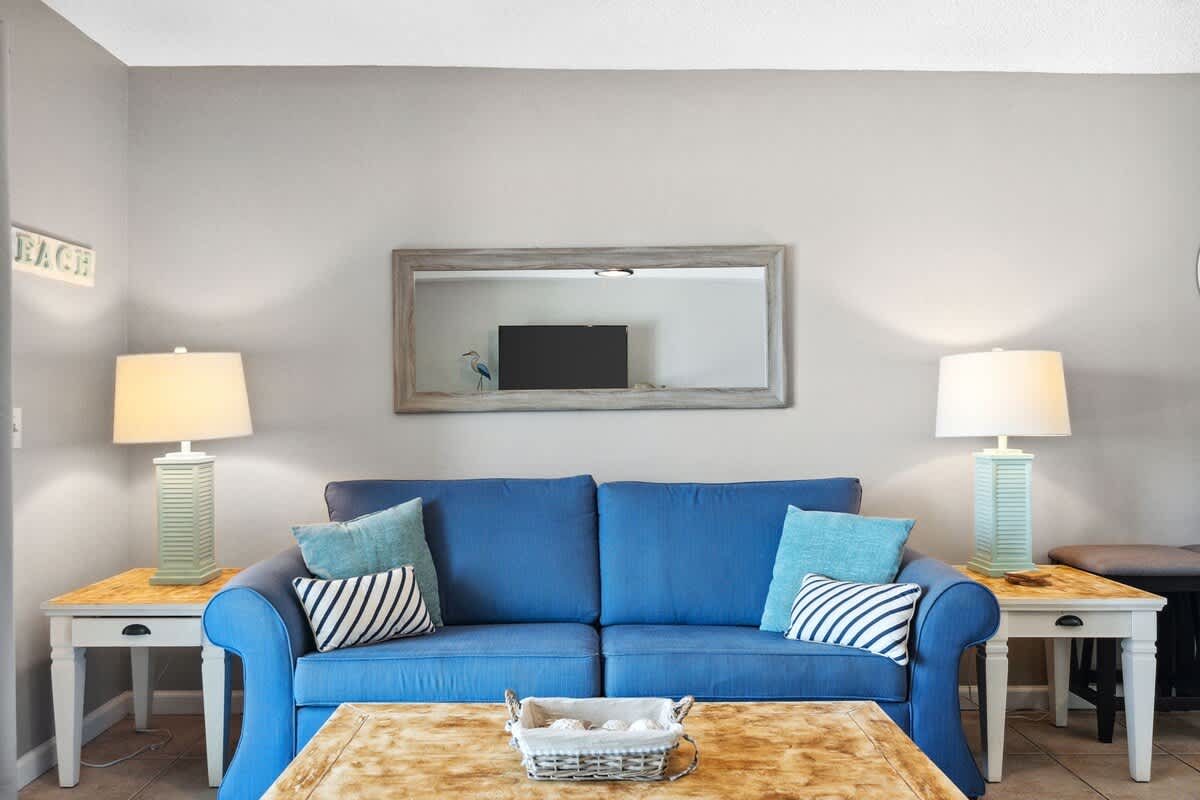 The Summit 817 – Living room with blue couch, lamps, mirror, and coffee table featuring decorative items.