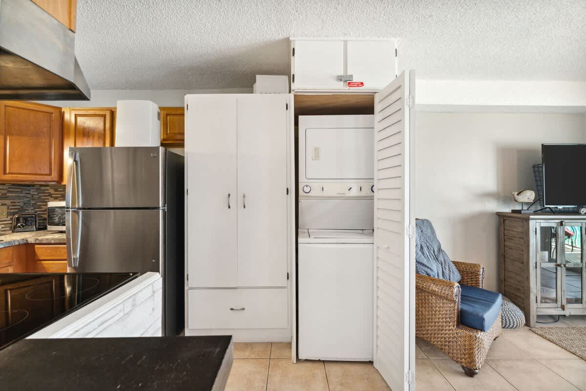 The Summit 817 – Kitchen area with stainless steel appliances, stacked washer and dryer, and wicker chair in living space.