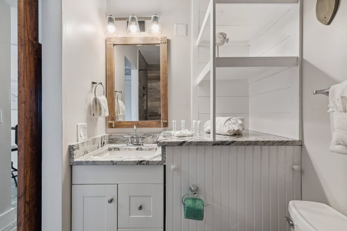 Top Of The Gulf 704 – Bathroom with granite countertop, large mirror, shelving, white towels, and toiletries.