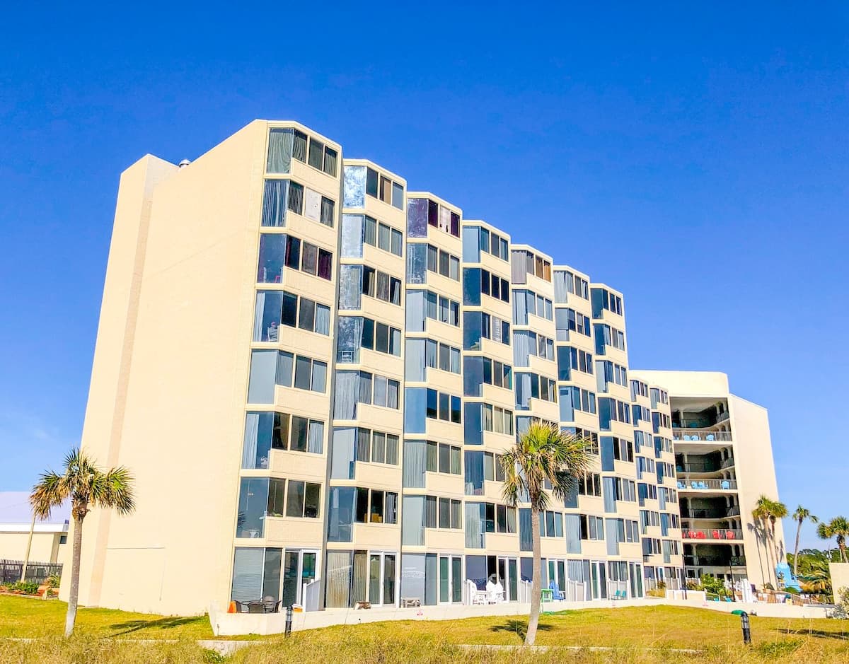 Top Of The Gulf 704 – Beachfront hotel with multiple stories, palm trees, and balconies overlooking the sea.