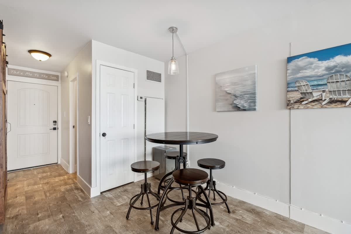Top Of The Gulf 704 – Entryway with a round table and chairs, beige walls, and beach-themed artwork.