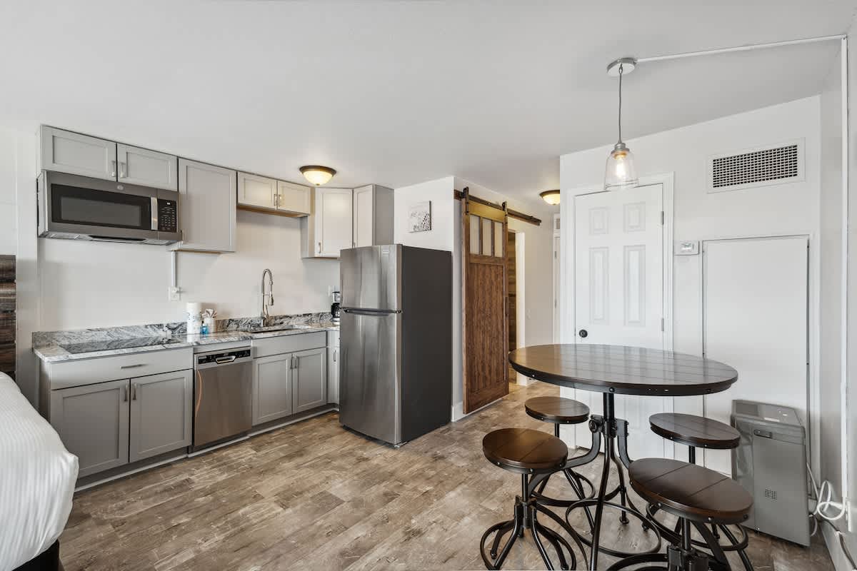 Top Of The Gulf 704 – Compact kitchen and dining area with a table, modern appliances, and wood-paneled sliding door.