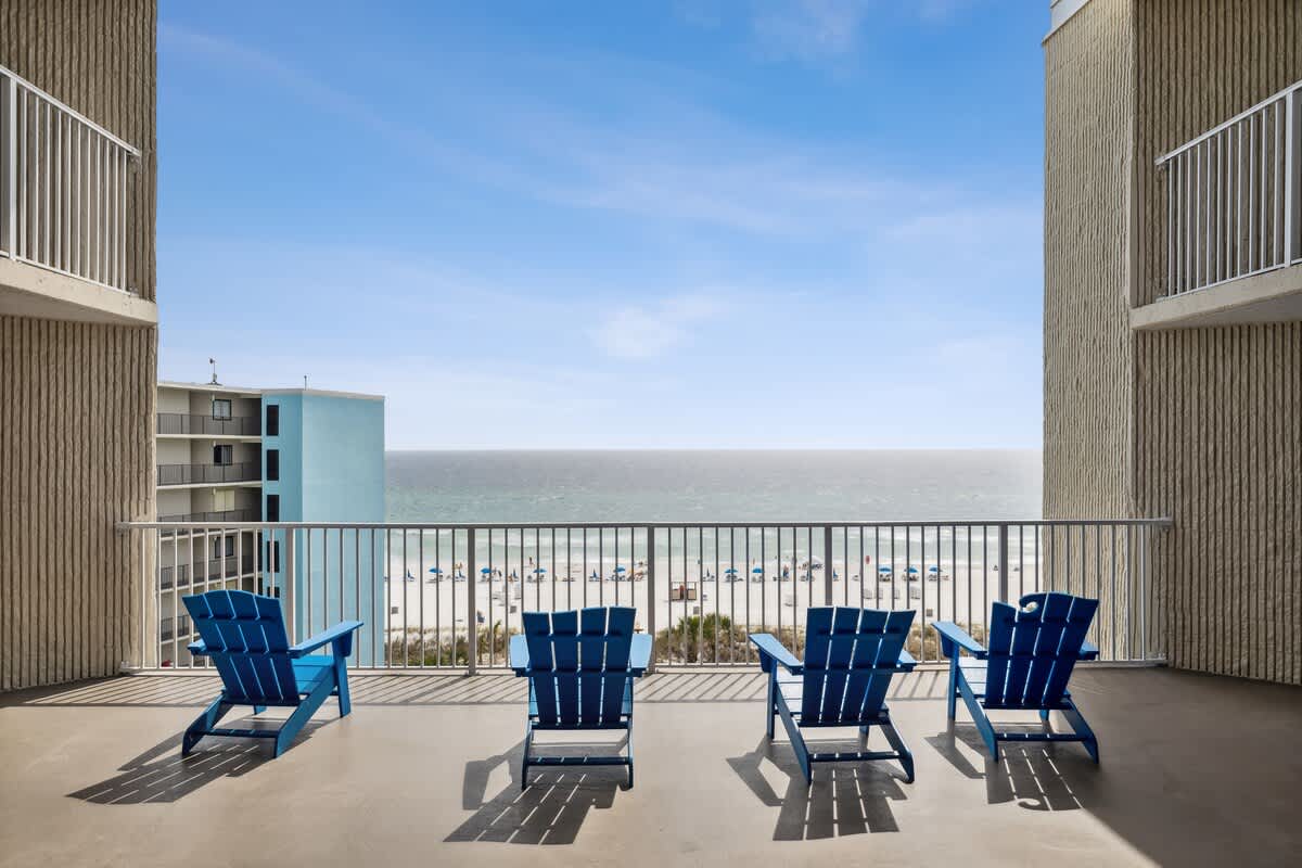 Top Of The Gulf 704 – Balcony with four blue chairs overlooking a sandy beach and ocean view.