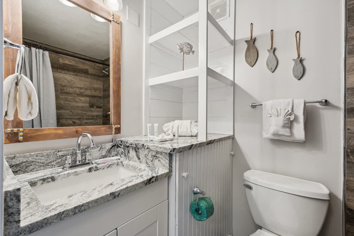 Top Of The Gulf 704 – Bathroom featuring a granite countertop, mirror, shower curtain, and decorative fish on the wall.