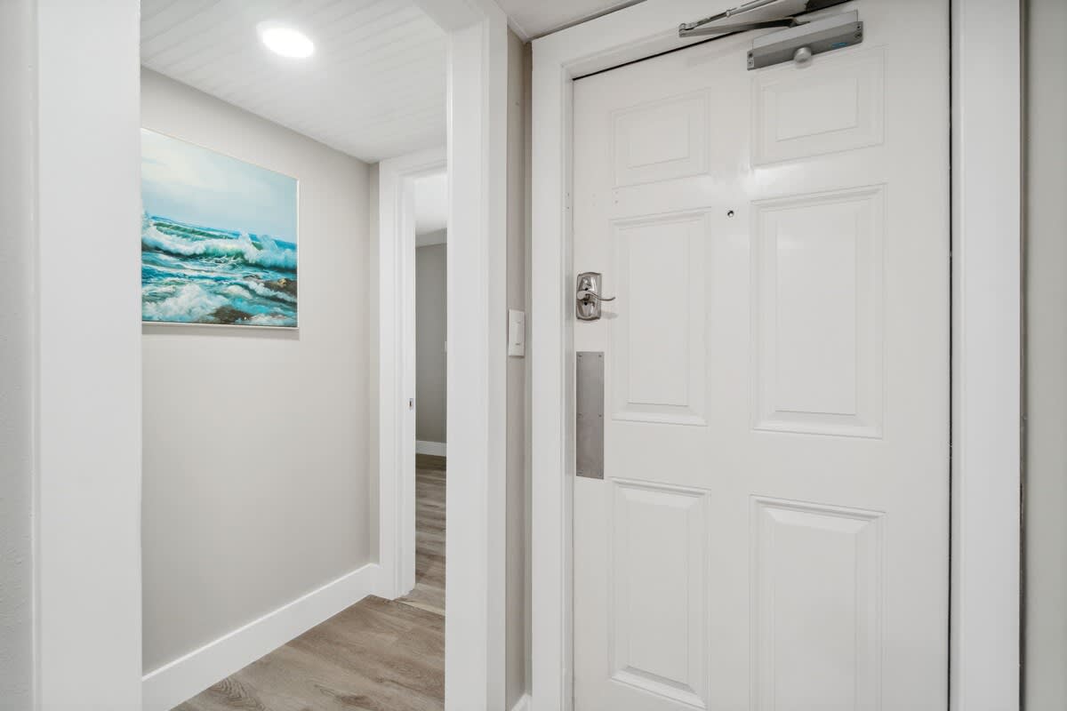 Moondrifter 502 – Entryway with white door, light wooden flooring, and ocean-themed artwork on the wall.