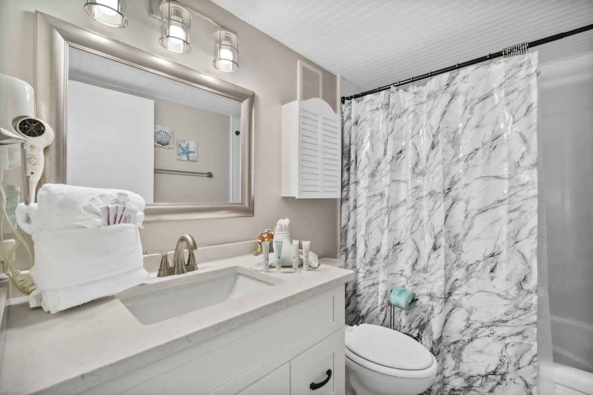 Moondrifter 502 – Bathroom with marble shower curtain, sink, mirror, decorative towels, and toiletries on countertop.