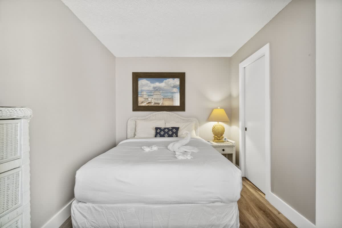 Moondrifter 502 – Cozy bedroom with a white bed, decorative towels, lamp, and beach-themed artwork on the wall.