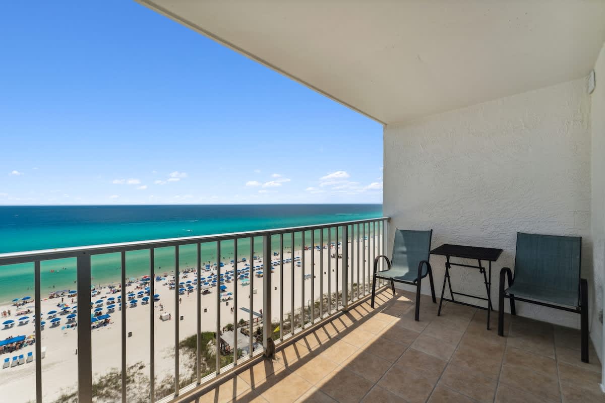 The Summit 1222 – Beachfront balcony with two chairs and a small table overlooking sandy beach and turquoise water.