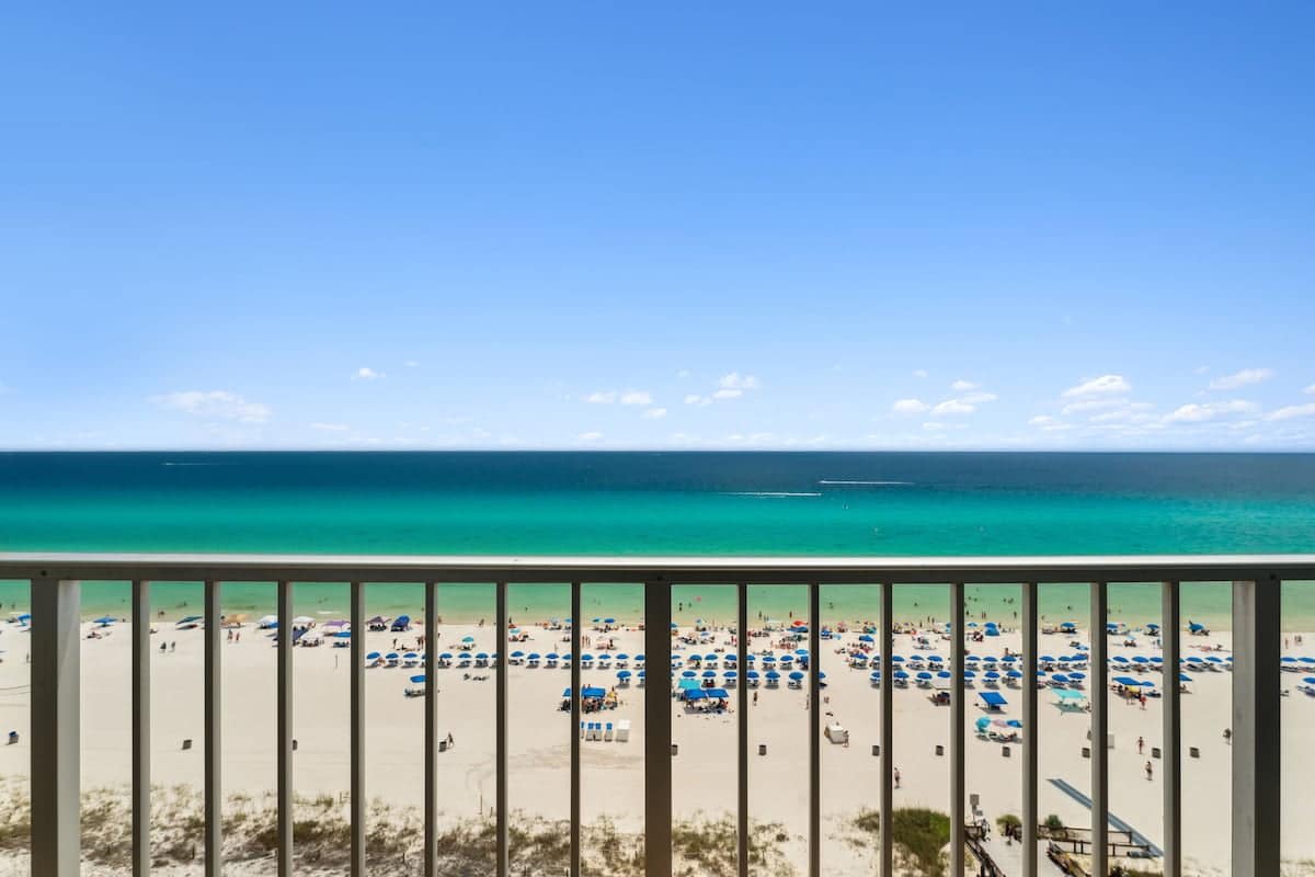 The Summit 1222 – Ocean view from balcony overlooking sandy beach with umbrellas and clear blue water.