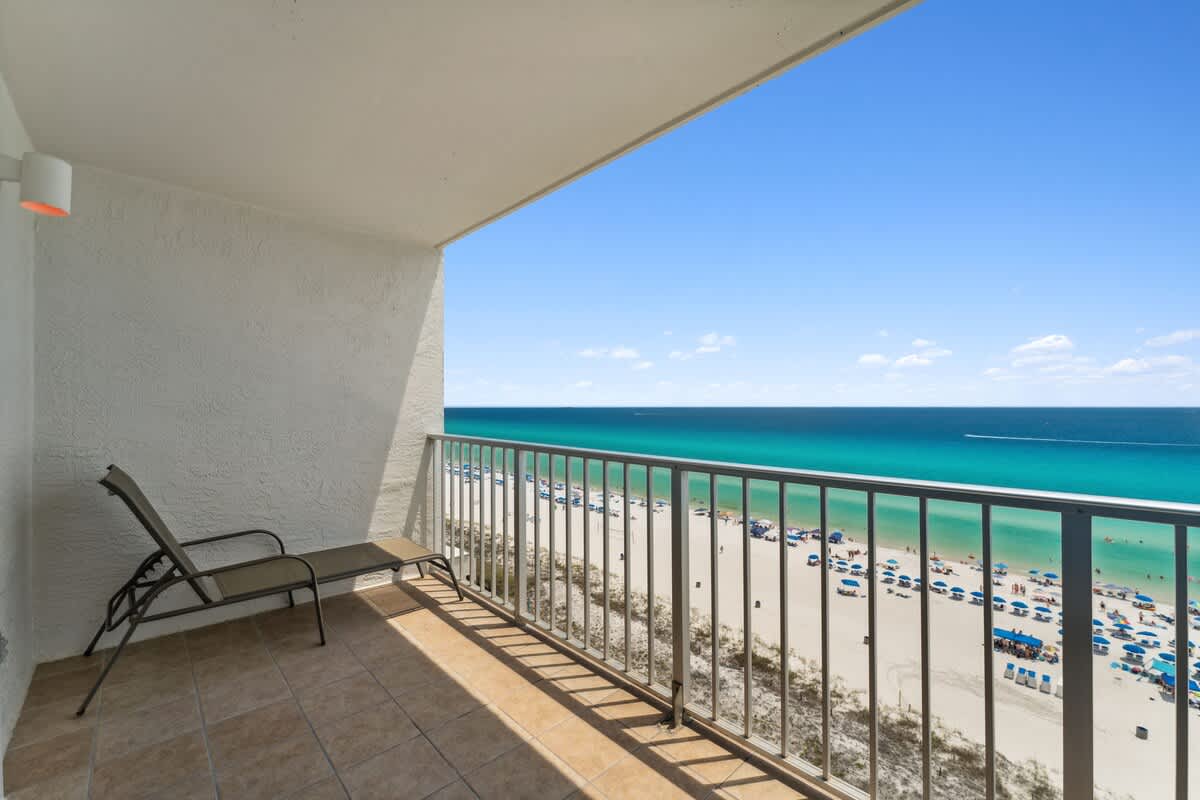The Summit 1222 – Balcony with a lounge chair overlooking a sandy beach and turquoise water.