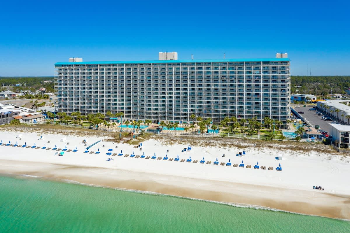 The Summit 1222 – High-rise vacation rental building overlooking a beach with palm trees and lounge chairs.