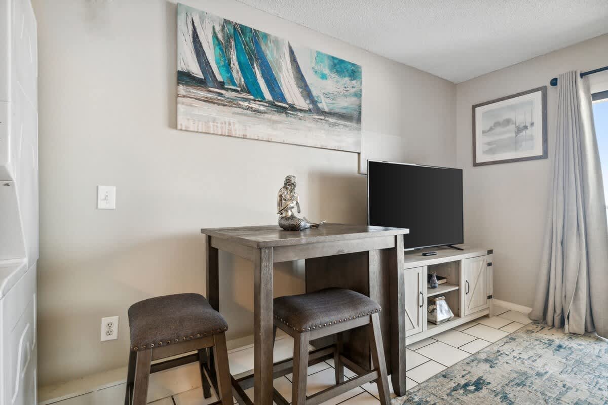 The Summit 725 – Cozy living area with a table, two stools, TV, and artwork featuring sailboats.