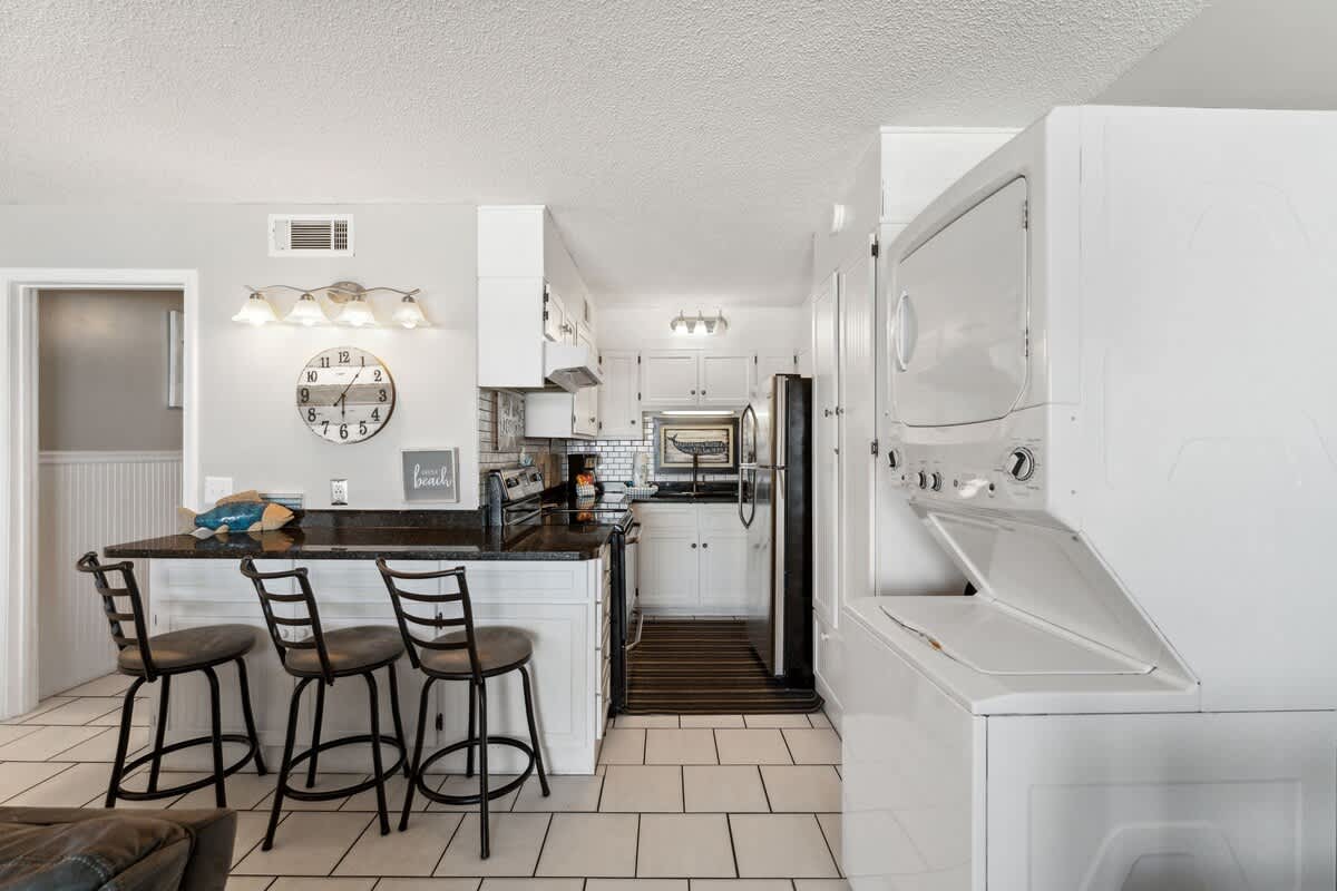 The Summit 725 – Modern kitchen with black countertops, white cabinetry, and laundry machines integrated into the space.