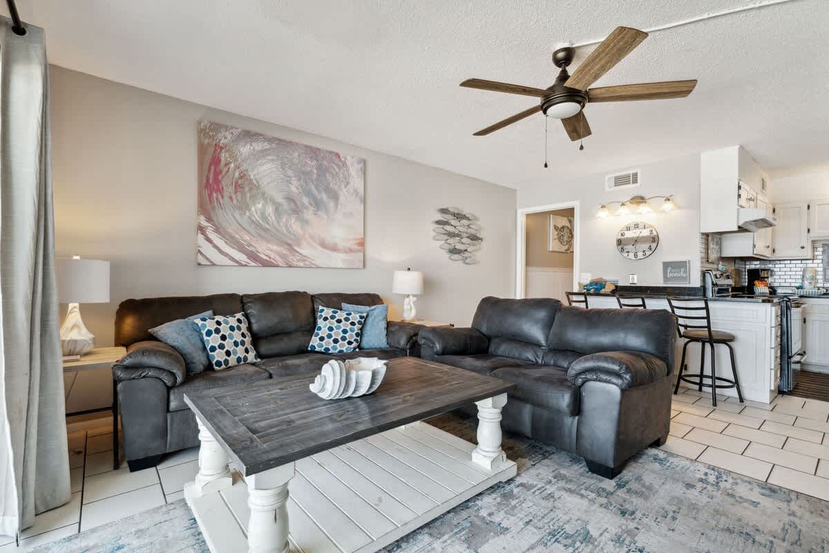 The Summit 725 – Living room with gray sofas, wooden coffee table, kitchen in background, and wall art.
