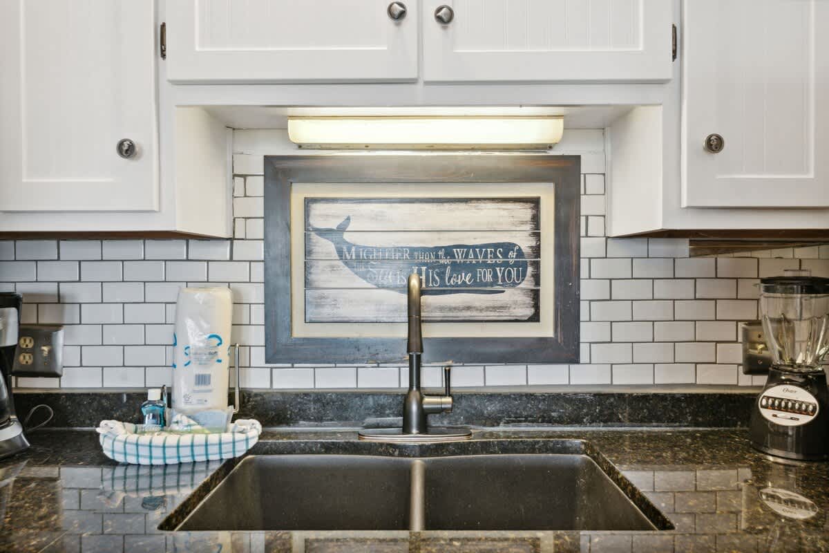The Summit 725 – Kitchen sink with black granite counter, white cabinets, and a whale-themed wall art above tile backsplash.