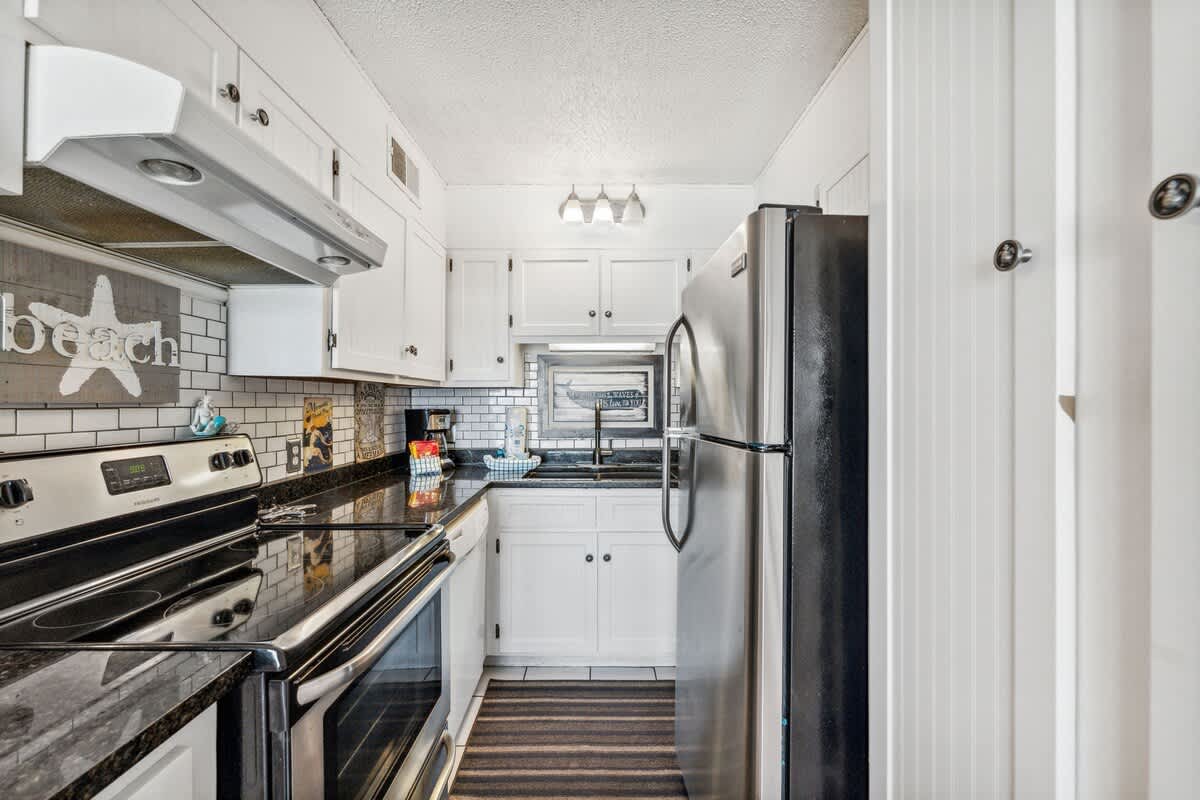The Summit 725 – Kitchen featuring black appliances, white cabinets, and a tile backsplash with a beach-themed decor.