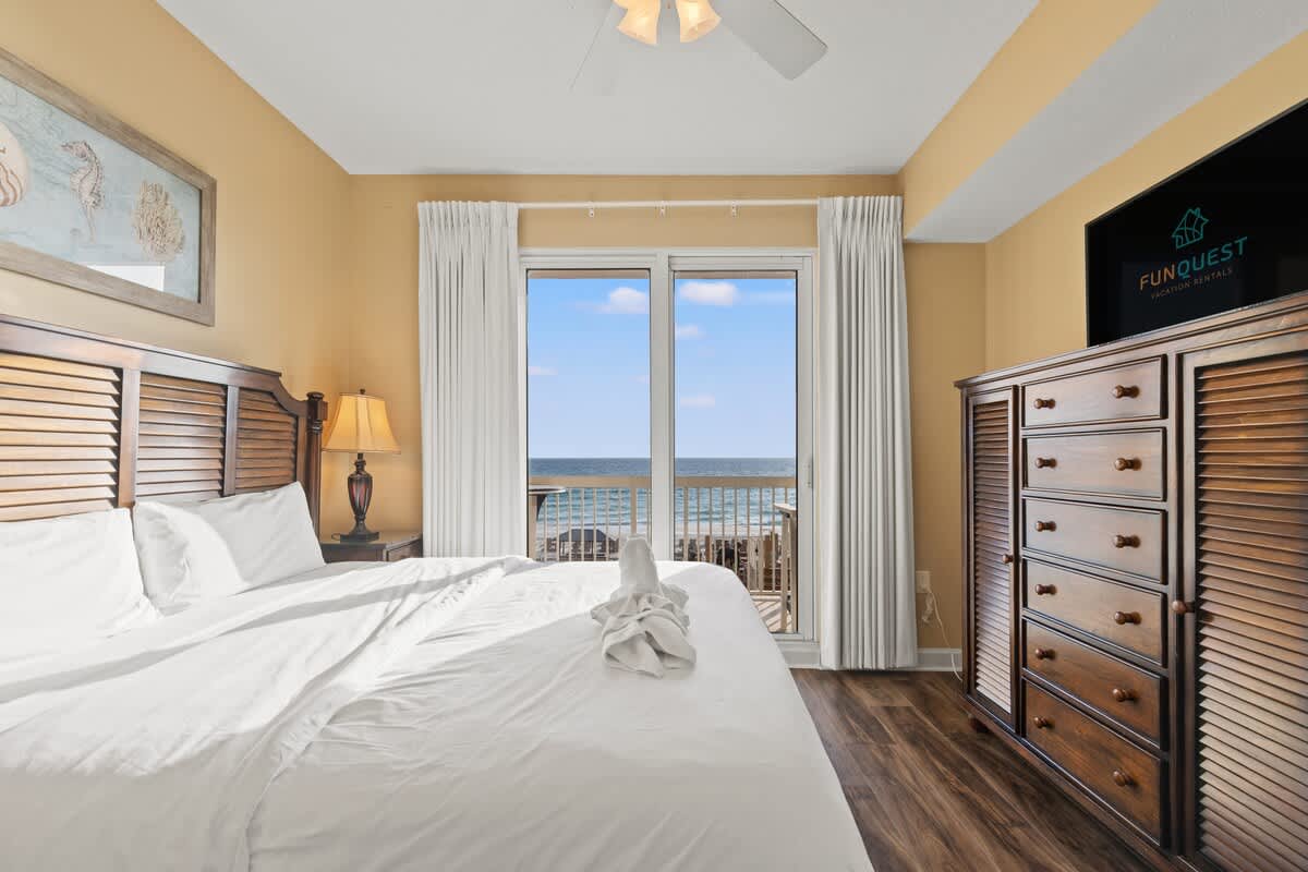 Seychelles 205 – Cozy bedroom with a sea view, featuring a wooden bed, dresser, and large sliding doors to a balcony.