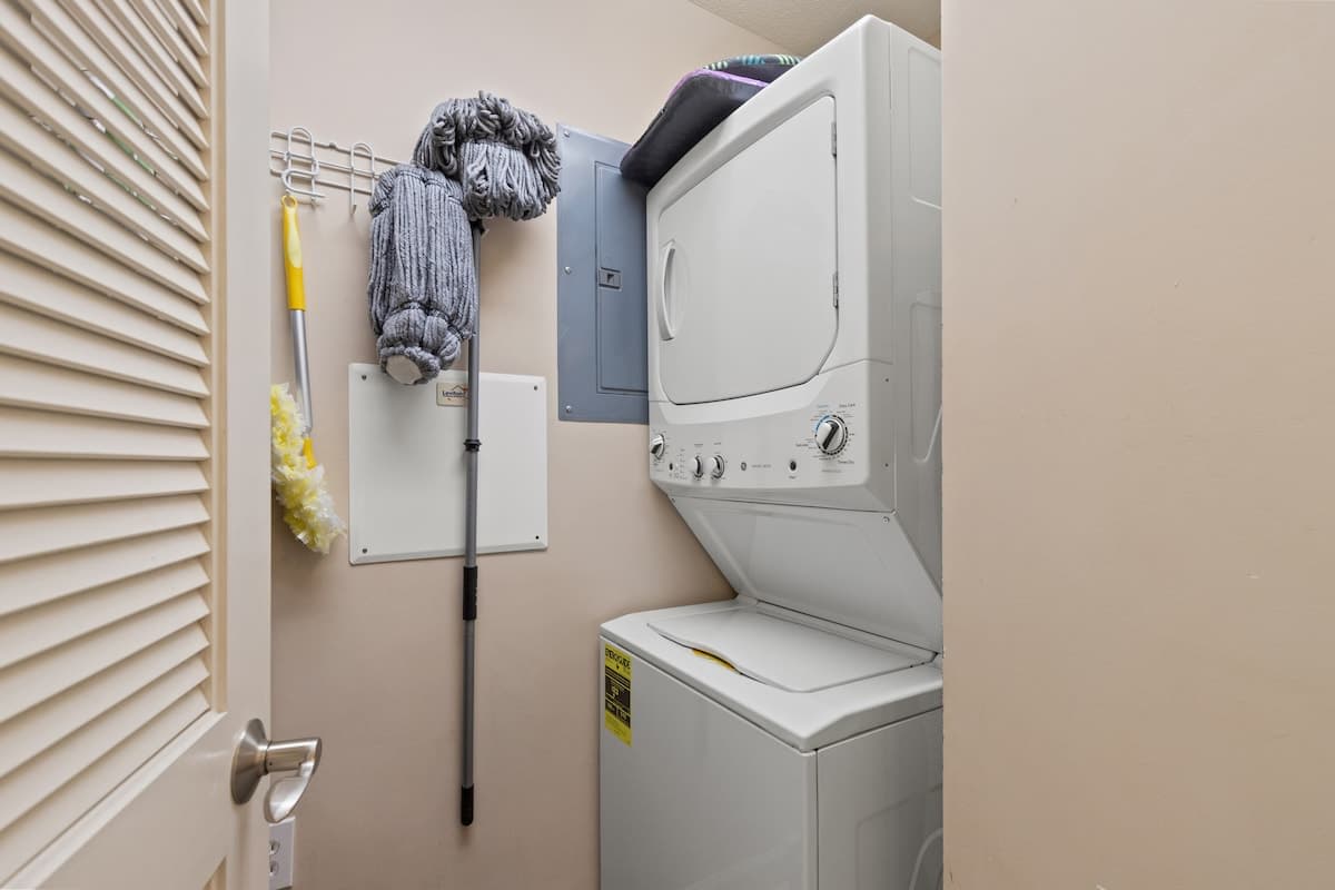 Seychelles 205 – Laundry area featuring a stacked washer and dryer, cleaning supplies on the wall, and beige walls.