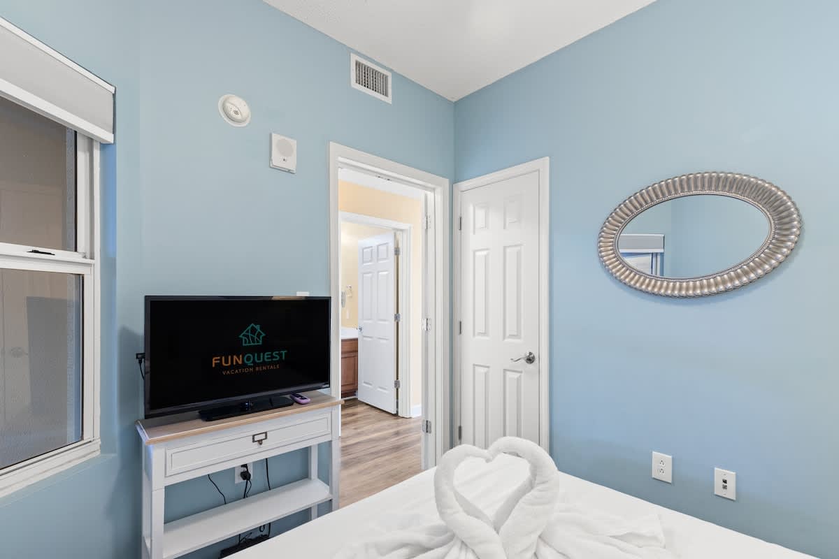 Seychelles 205 – Bedroom with blue walls, a TV, and a towel shaped like a heart on the bed.