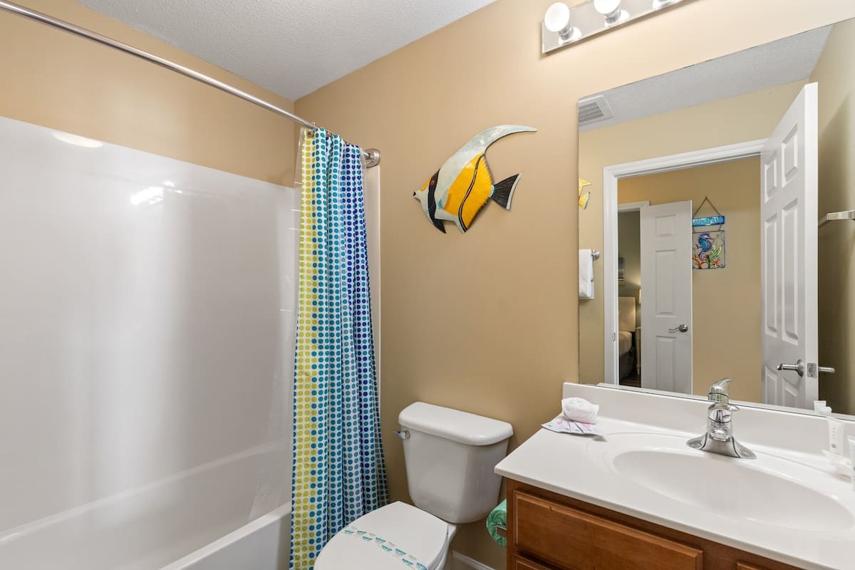 Seychelles 205 – Bathroom with a shower, decorative fish, mirror, and sink with wooden cabinet.