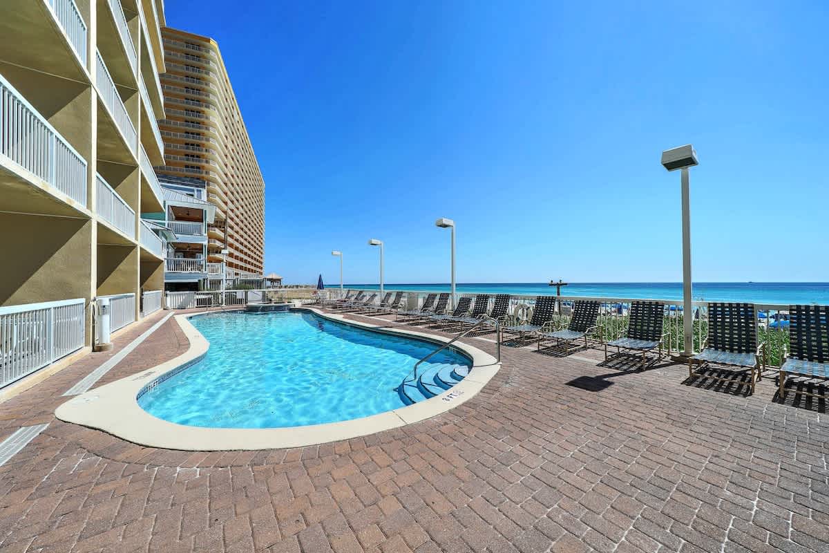 Seychelles 205 – Poolside area with lounge chairs and ocean view, surrounded by a tall building and clear blue sky.