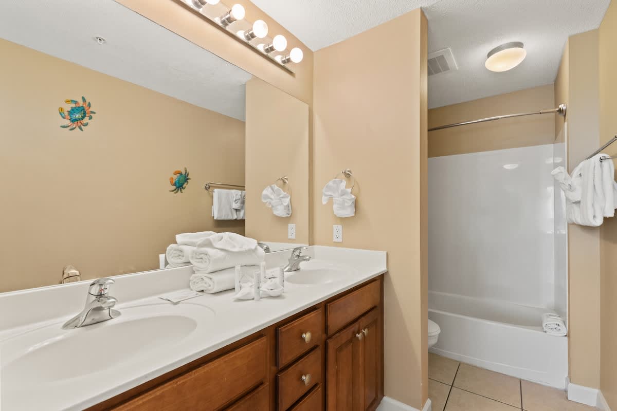 Seychelles 205 – Bathroom with double sink, mirrors, beige walls, and a shower/tub combination.
