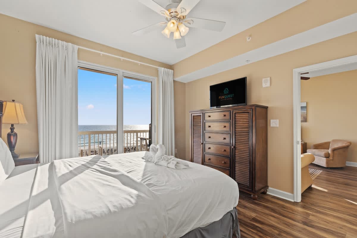 Seychelles 205 – Bright bedroom with a view of the beach, featuring a queen bed, dresser, and a TV.