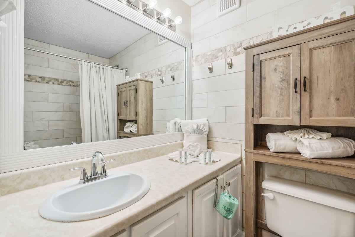 Top Of The Gulf 613 – Bathroom with a sink, wooden cabinet, towels, and decorative mirror.