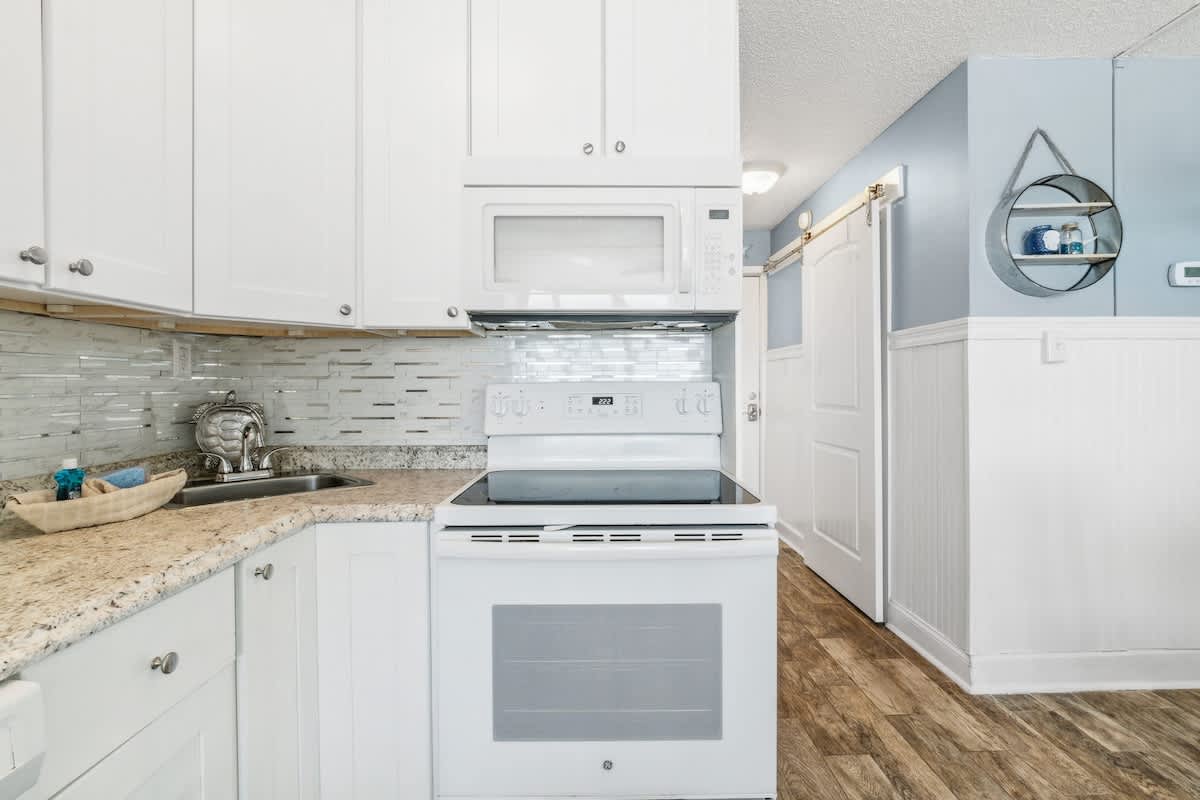 Top Of The Gulf 613 – Compact kitchen featuring white cabinets, granite countertops, and modern appliances.