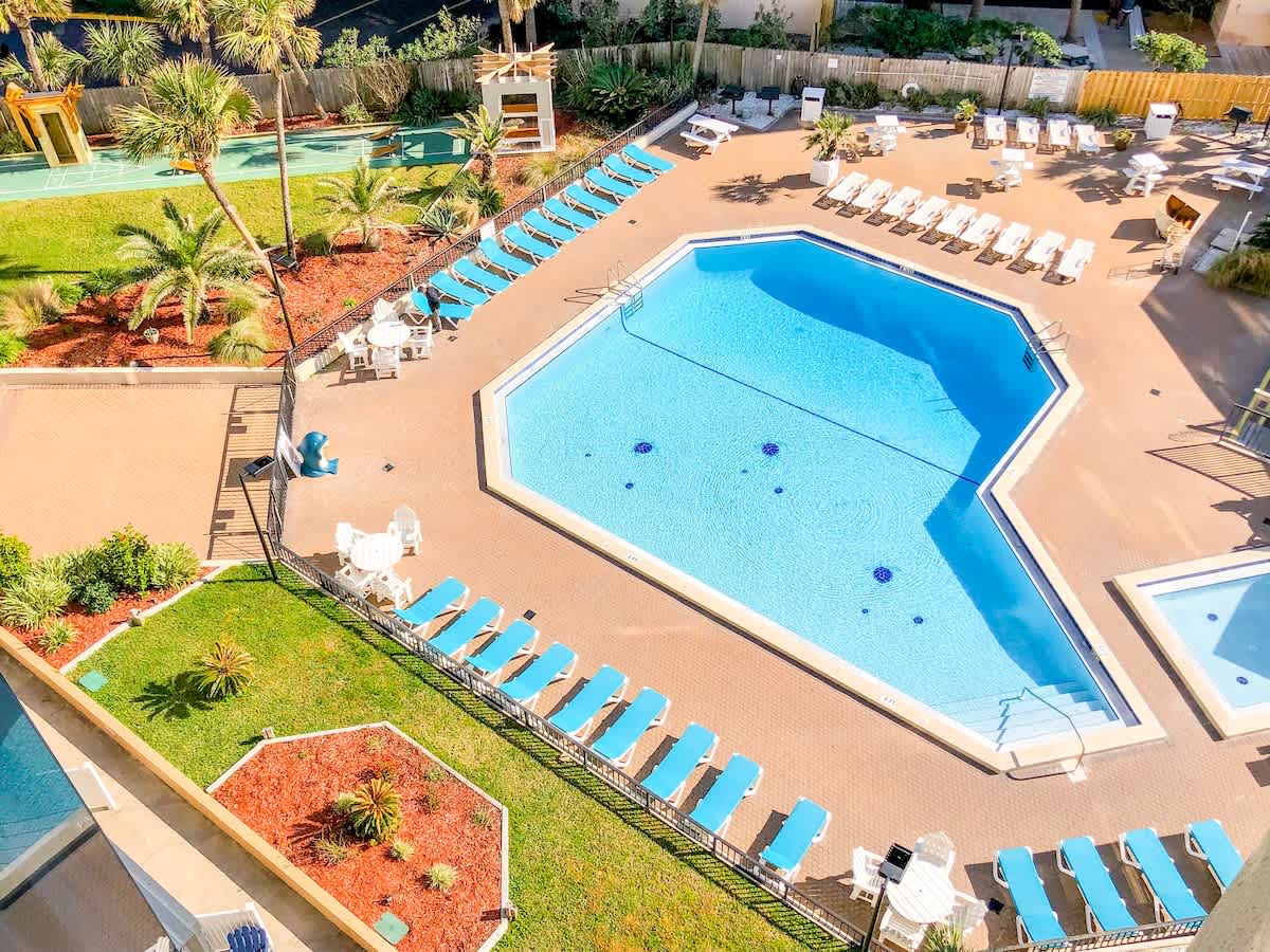 Top Of The Gulf 613 – Aerial view of a pool area with lounge chairs, palm trees, and a hot tub.