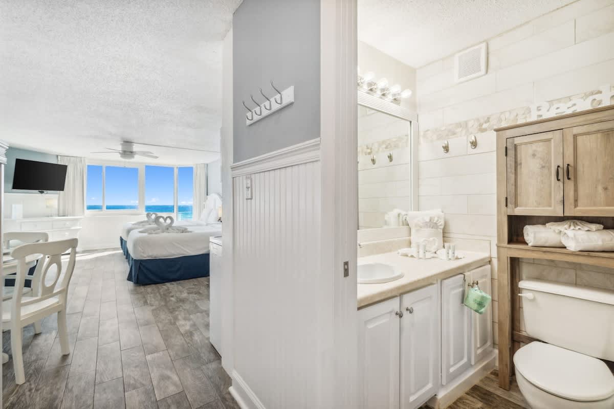 Top Of The Gulf 613 – Bright studio with a bathroom, kitchenette, and ocean view through large windows.